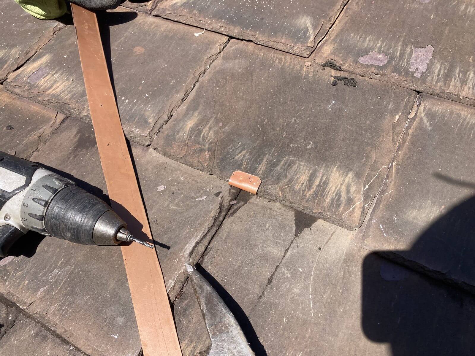 Copper clip nailed between slate tiles during a roof repair